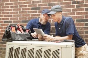 Two HVAC technicians reviewing a tablet during an AC compressor replacement job.